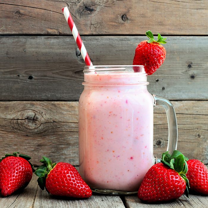 Healthy strawberry smoothie in a mason a jar glass with scattered berries over a rustic wood background