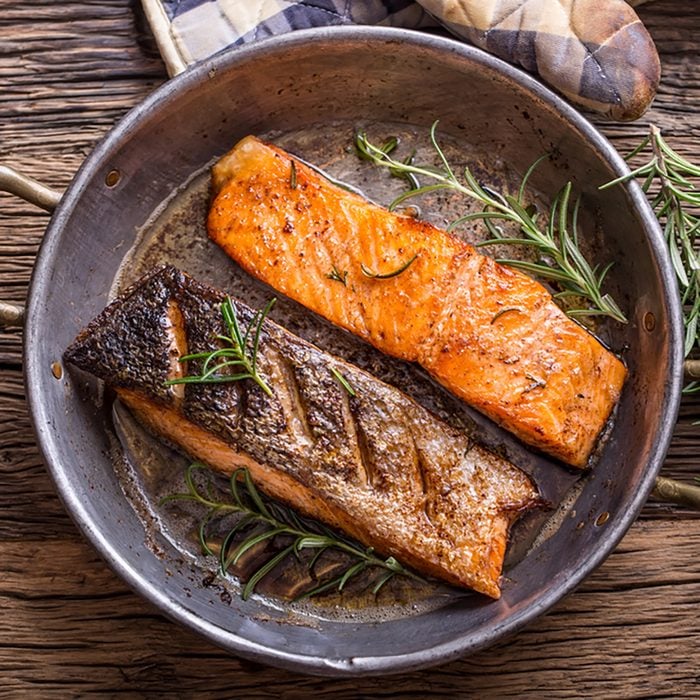 Grilled salmon fillets and herb decoration in old roasted pan.