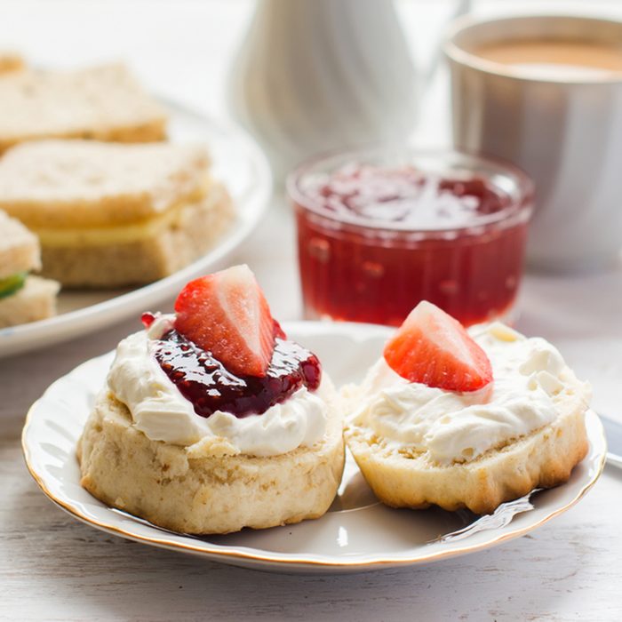 Traditional English afternoon tea: scones with clotted cream and jam, strawberries, with various sandwiches on the background