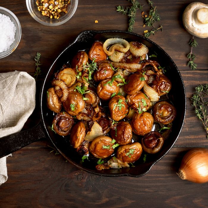 Roasted mushrooms with onion in frying pan over wooden background