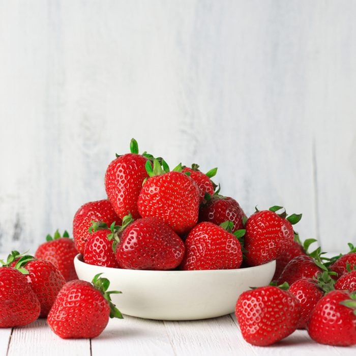 Heap of fresh strawberries in ceramic bowl on rustic white wooden background.