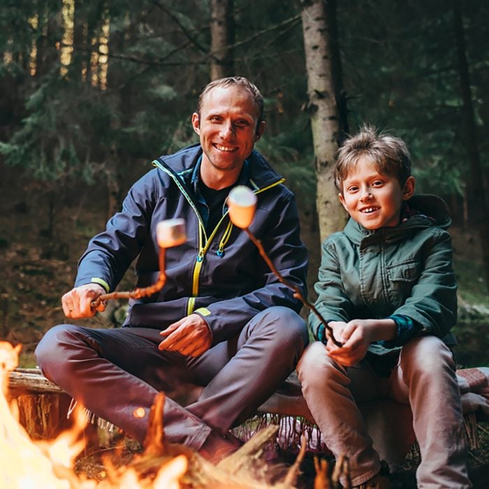 Father and son roast marshmallow candies on the campfire in forest.