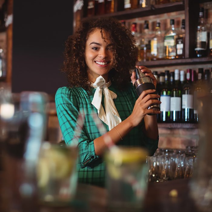 Portrait of female bartender mixing a cocktail drink in cocktail shaker at counter