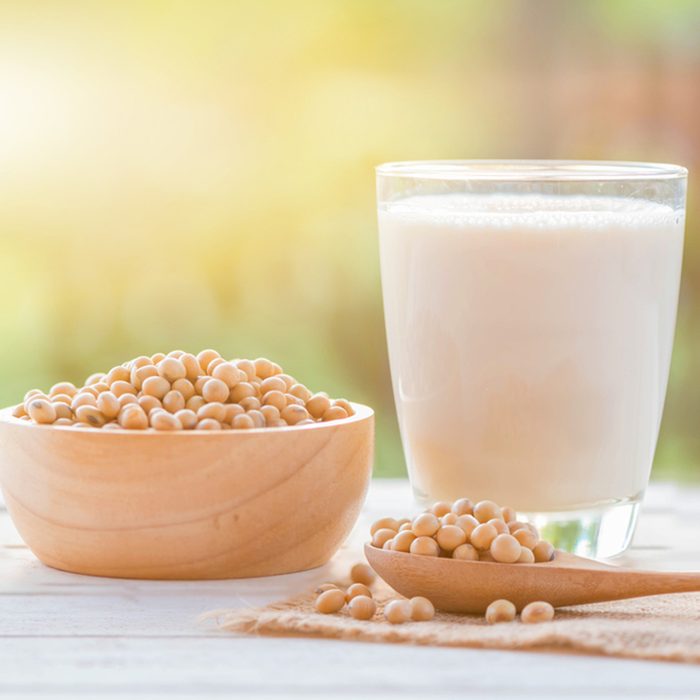 Soy milk in glass and soy bean on spoon it on white table background with lighting in the morning