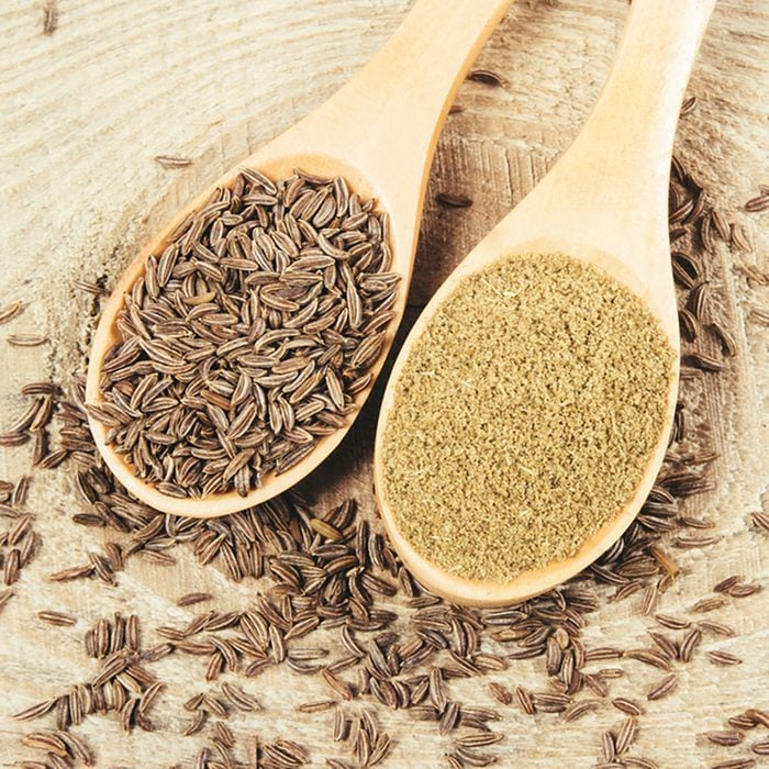 Ground cumin in a spoon and whole cumin on the wooden background.