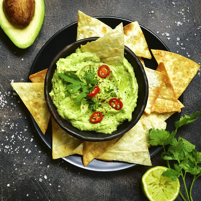 Avocado dip guacamole with tortilla chips in a black bowl on a dark slate or metal background.Top view with copy space.