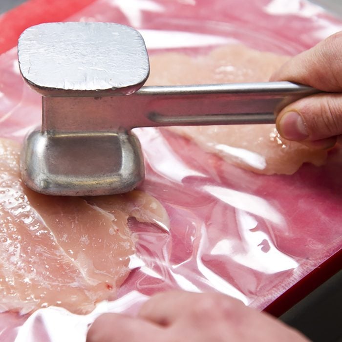 Tenderizing the chicken meat with a mallet - Preparing homemade chicken kiev in a kitchen