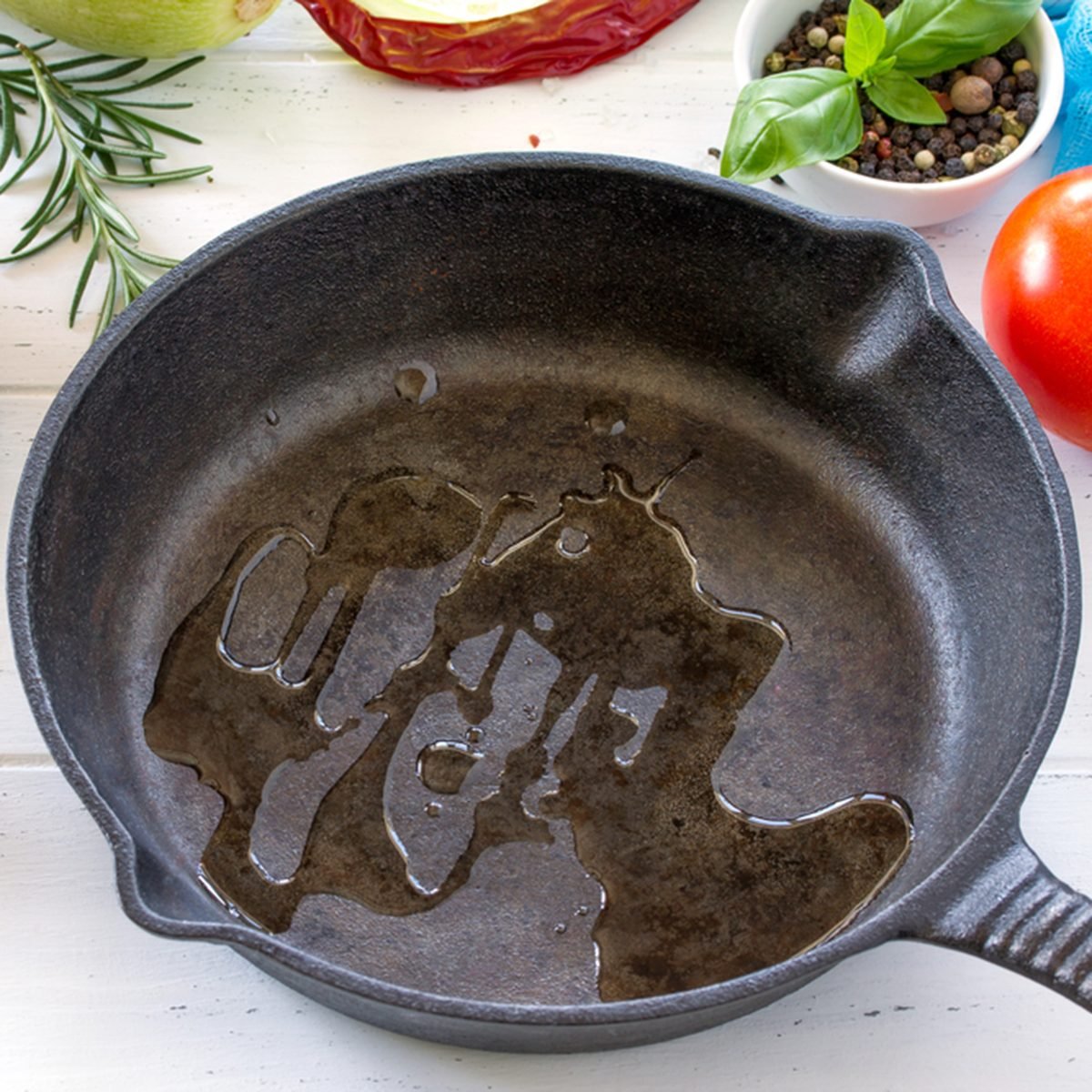 Frying pan made of cast iron, various fresh vegetables and spices on a white wooden kitchen table.