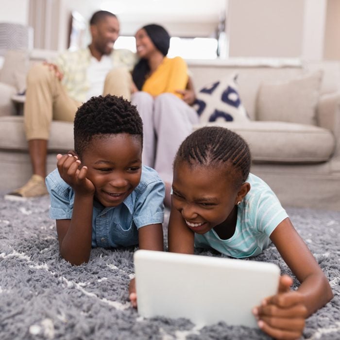 Smiling children using digital tablet while parents siting on sofa at home