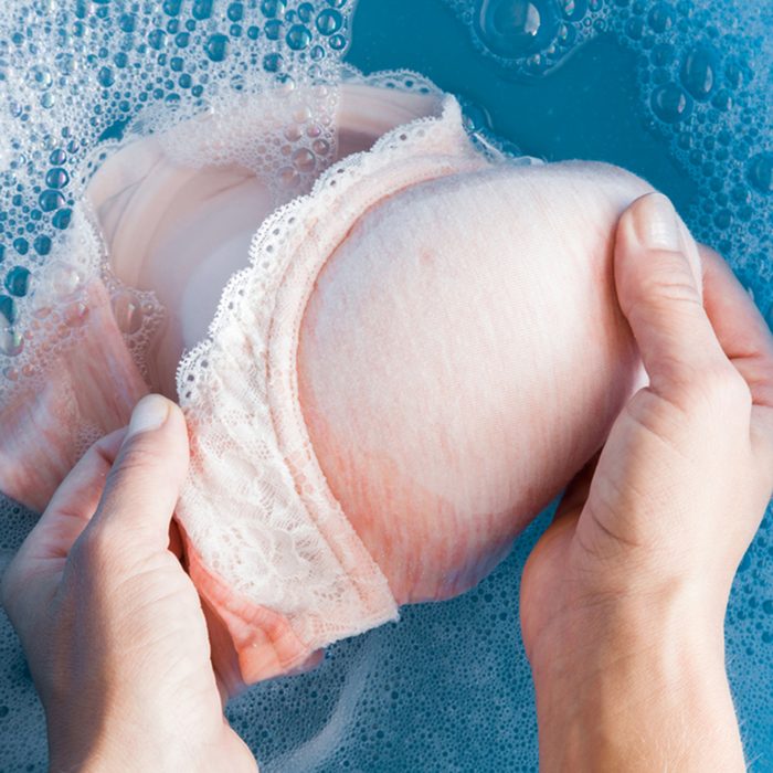 Hands washing light pink women's bra in the blue basin.