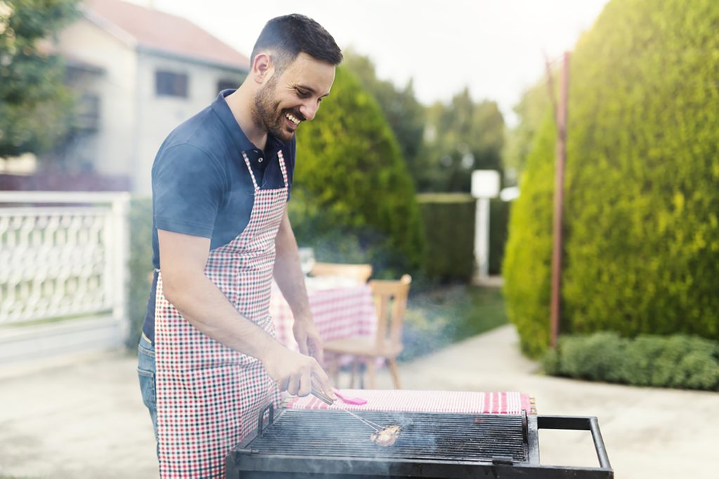 Young handsome chef smiling and cleaning grill