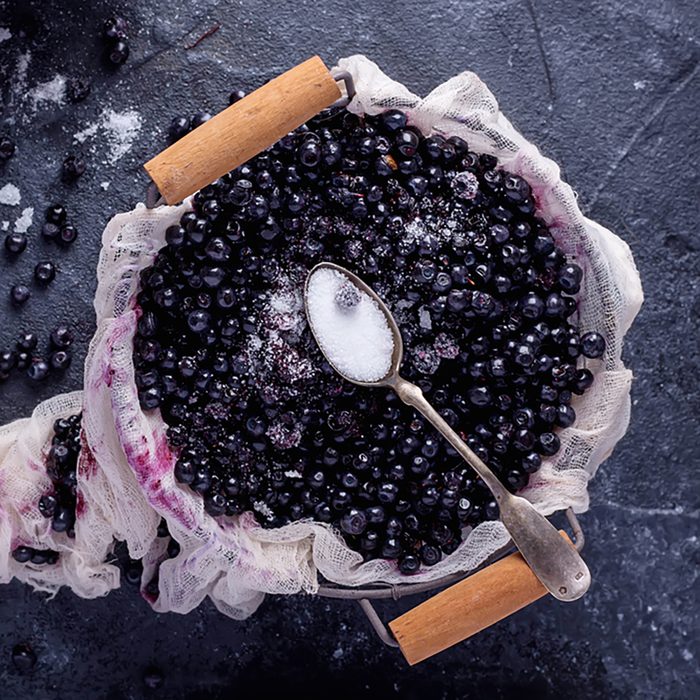 Wild blueberries in metal basket served with sugar on rustic stone board decorated with napkin