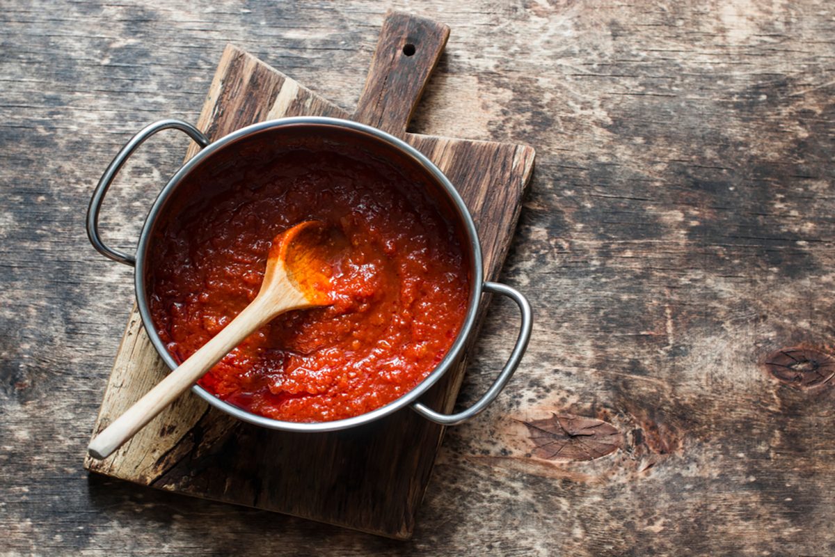 Classic homemade tomato sauce in the pan on a wooden chopping board on brown background, top view.