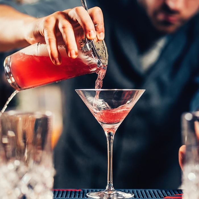 Close up details of barman pouring vodka cosmopolitan cocktail in martini glass;