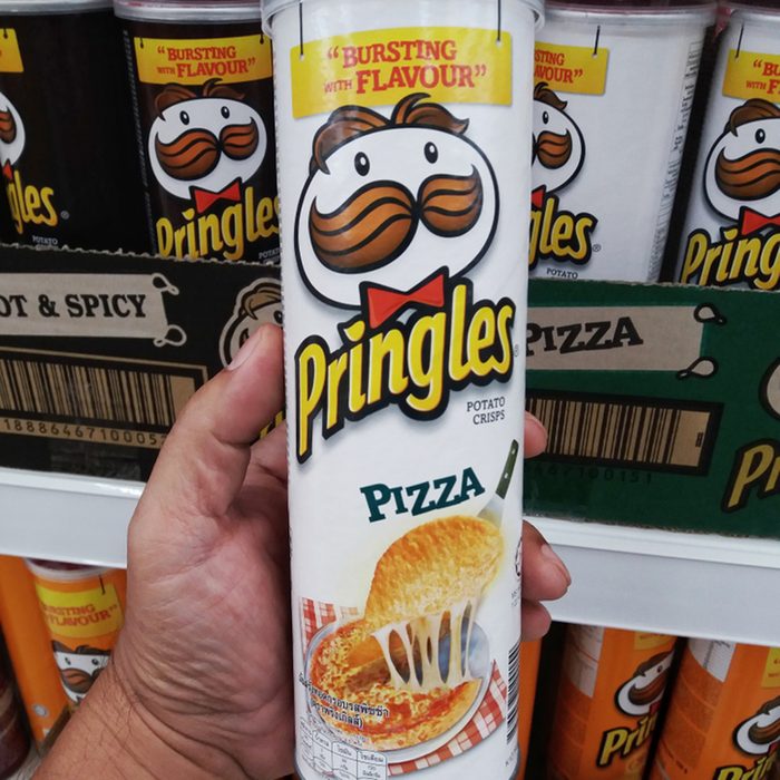 Hand holding a tube of pizza flavour Pringles potato chips. Pringles is an American brand of snack chips owned by Kellogg's