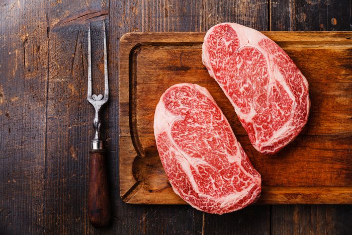 Raw fresh marbled meat Steak Ribeye Black Angus and meat fork on wooden background copy space; Shutterstock ID 651752392