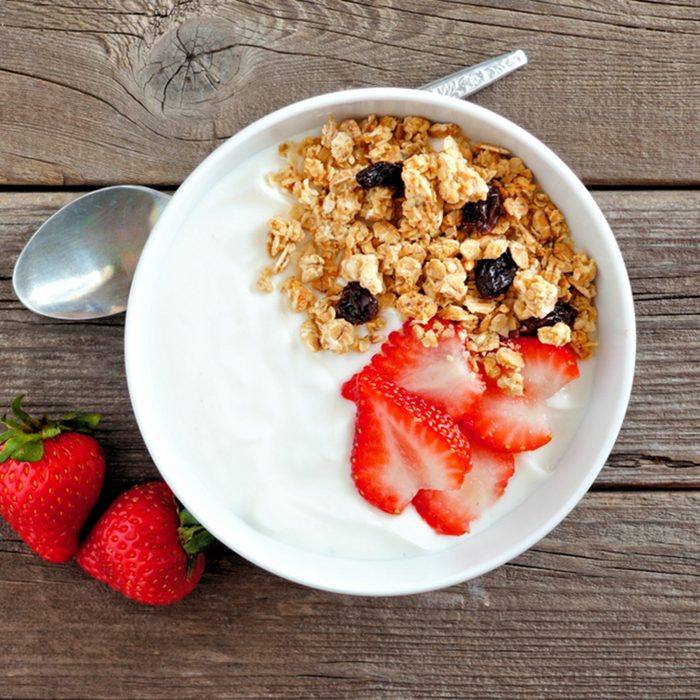 Bowl of yogurt with strawberries and granola over a rustic wood background.