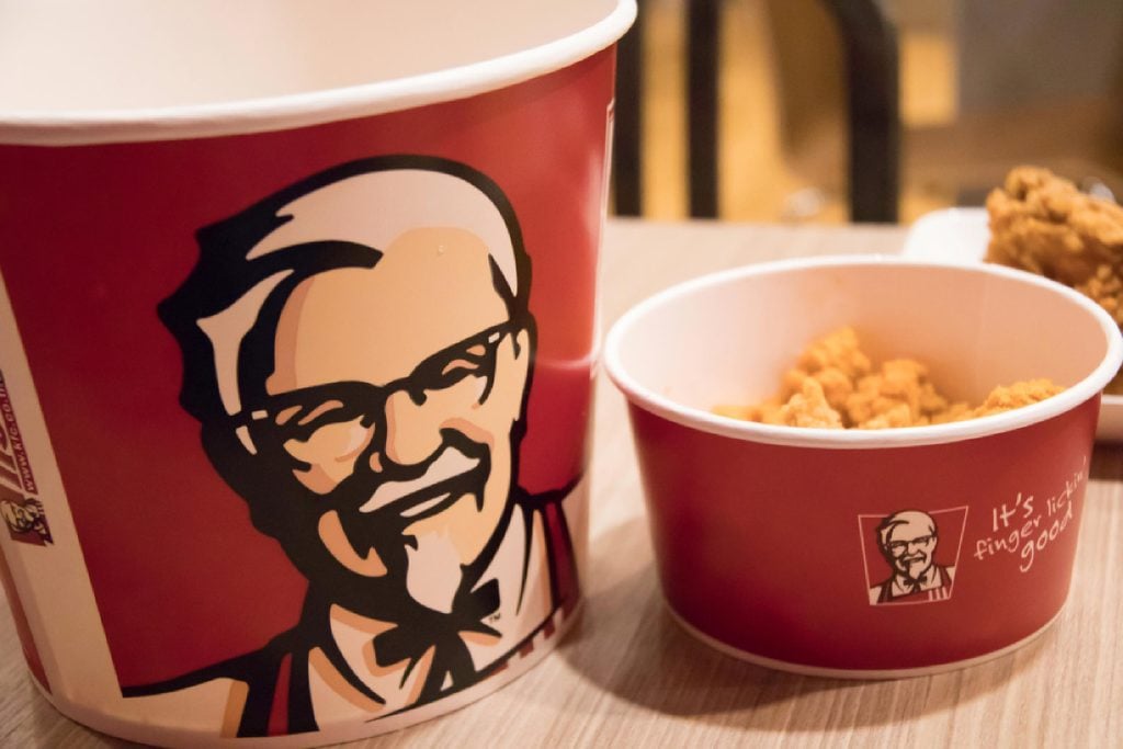 Kentucky Fried Chicken bucket filed with chicken beside a bowl of fries