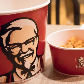Kentucky Fried Chicken bucket filed with chicken beside a bowl of fries
