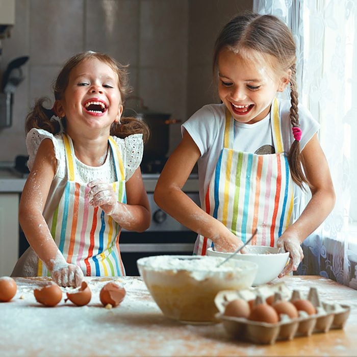 happy sisters children girls bake cookies, knead dough, play with flour and laugh in the kitchen