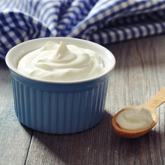 Greek yogurt in a ceramic bowl with spoons on wooden background