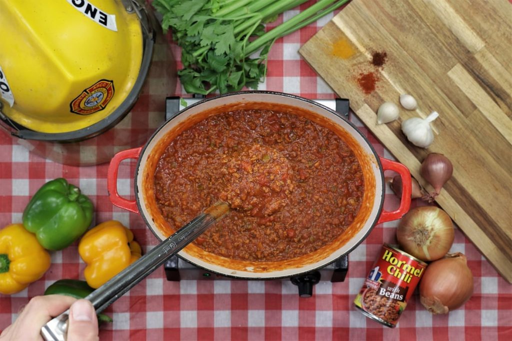Hormel chili in a slow cooker beside a firefighter's hat