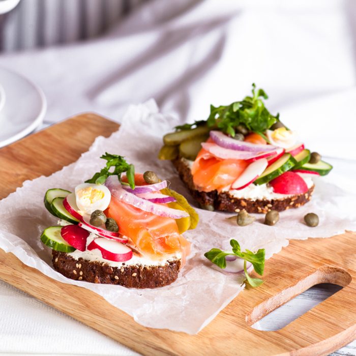 Fresh organic homemade sandwich smorrebrod with cereals dark rye grain bread toasts, salted salmon and black coffee mug on wooden board.