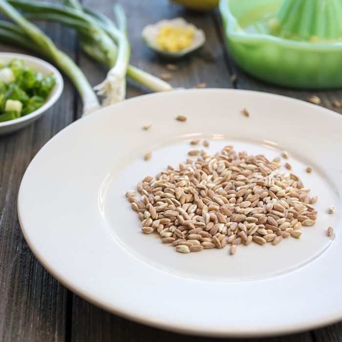 Plate of uncooked farro grains with onions, lemons, butter and rind as ingredients for a recipe;