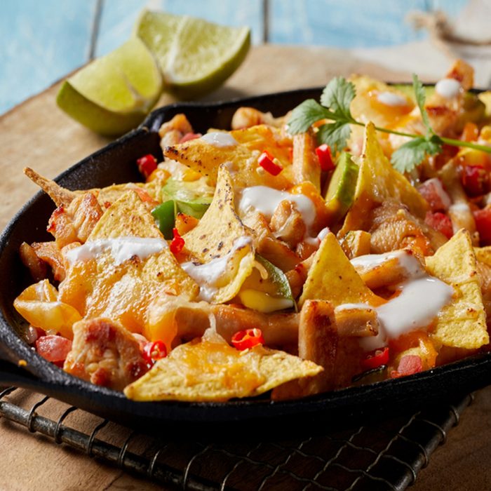 Spicy Mexican chicken with nachos and fresh herbs drizzled with cream and served in a rustic skillet in a close up view
