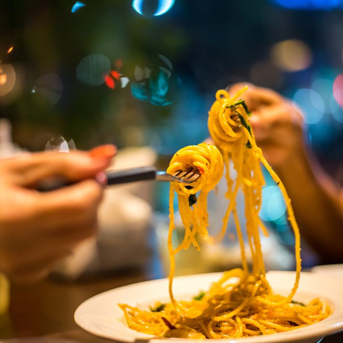 Spaghetti on a fork. Hand of two woman rolling spaghetti and keeping on a fork for eat.