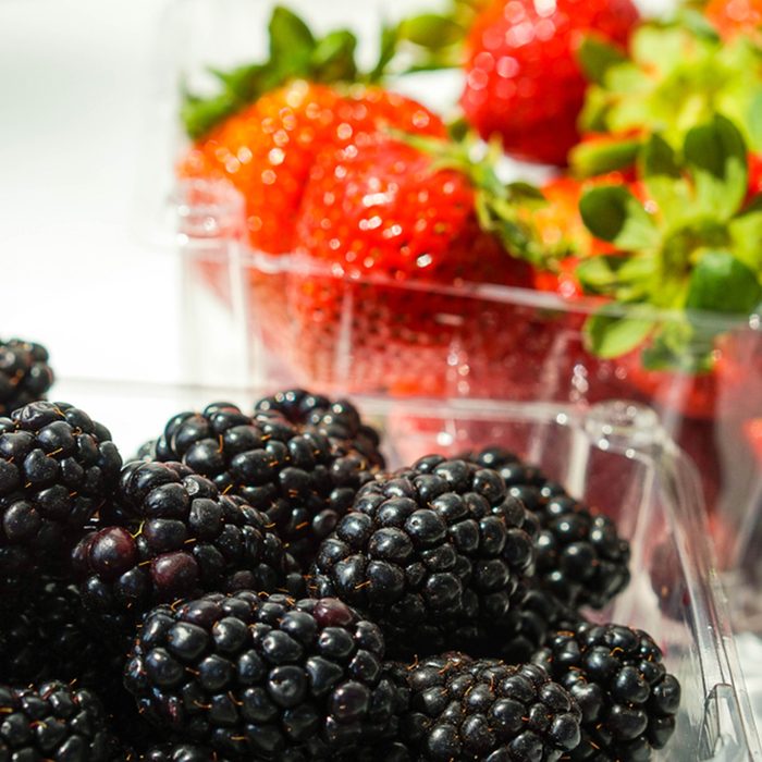 Blackberries in plastic container with strawberries in the background