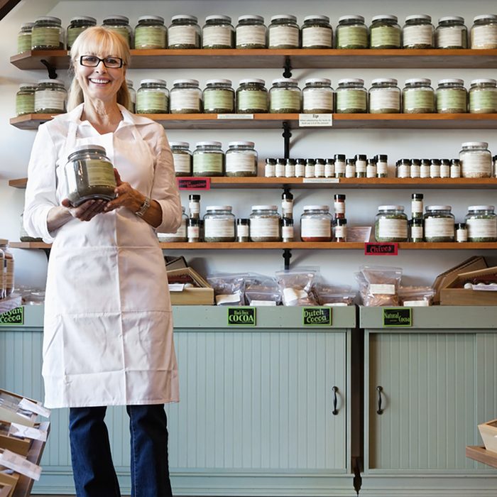 Portrait of a happy senior merchant standing with spice jar in store