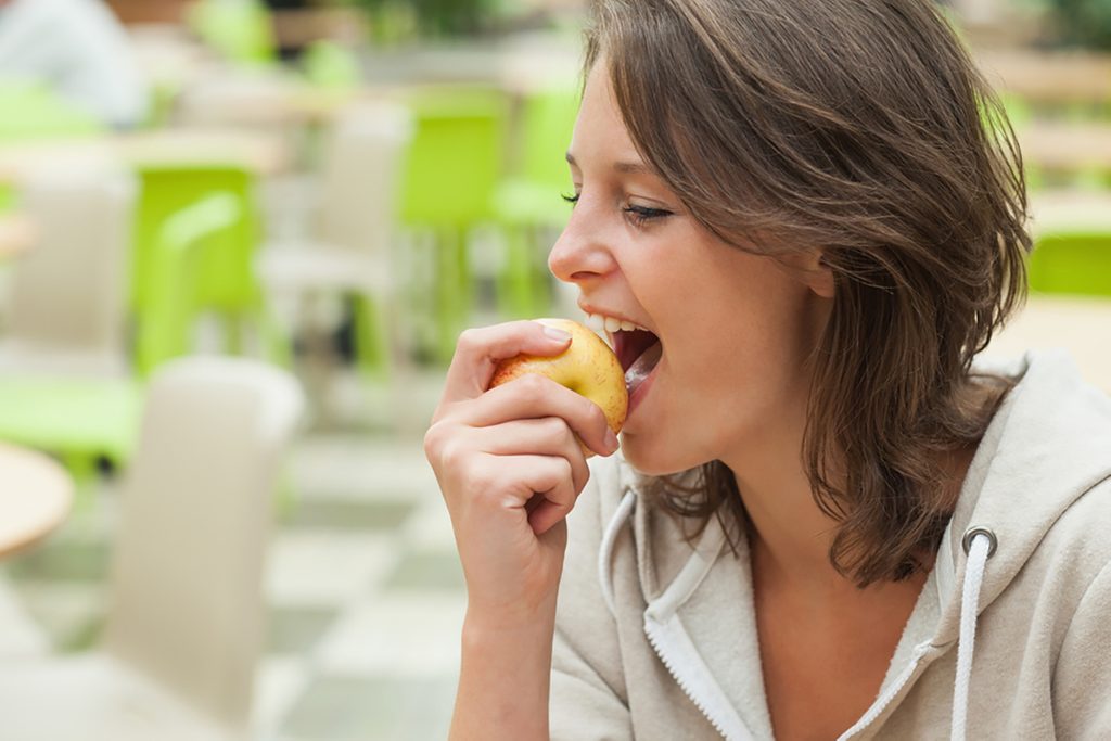 Close-up side view of a young woman eating apple in the cafeteria