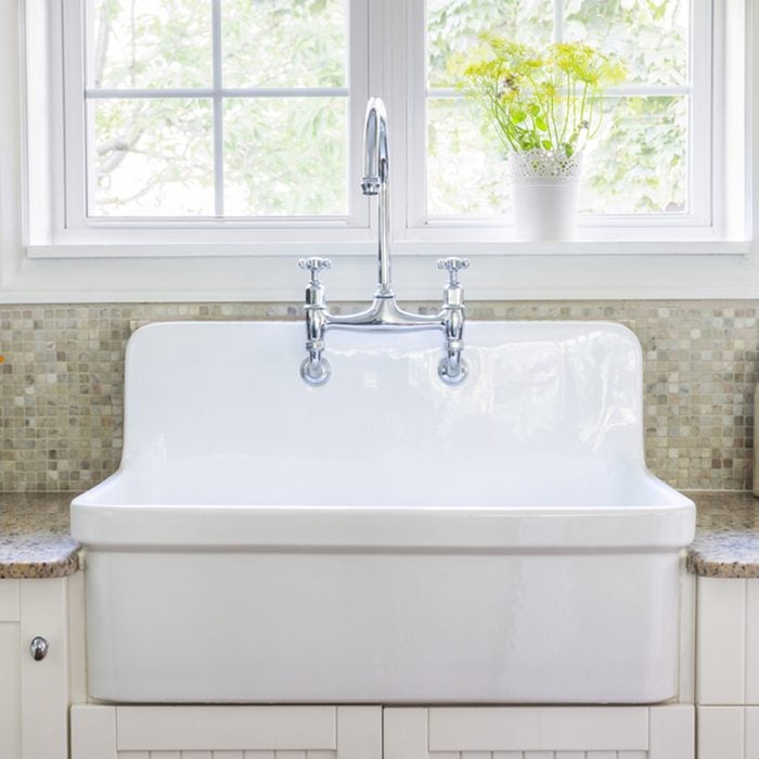 Kitchen interior with large rustic white porcelain sink and granite stone countertop under sunny window