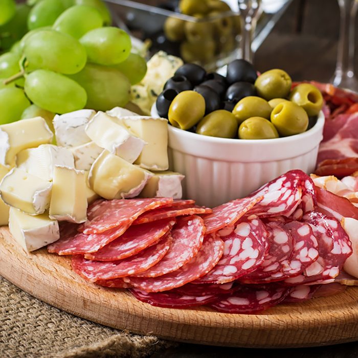 Antipasto catering platter with bacon, jerky, salami, cheese and grapes on a wooden background