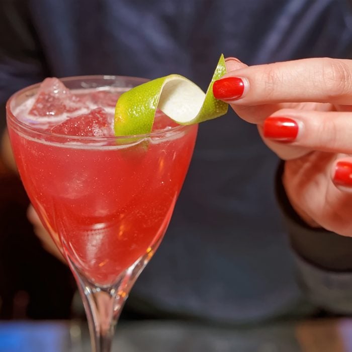 Female bartender is decorating a cocktail with lime zest