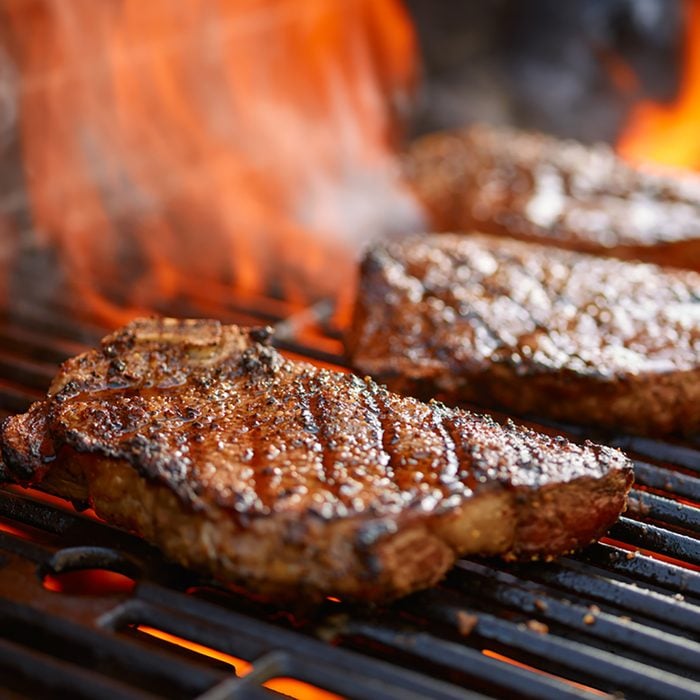 grilling steaks on flaming grill