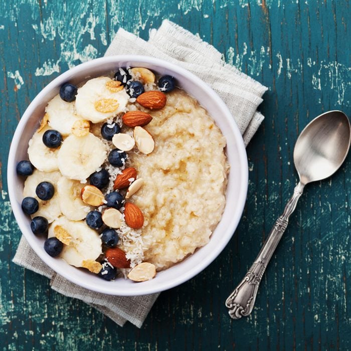 Bowl of oatmeal porridge with banana, blueberries, almonds, coconut and caramel sauce on teal rustic table