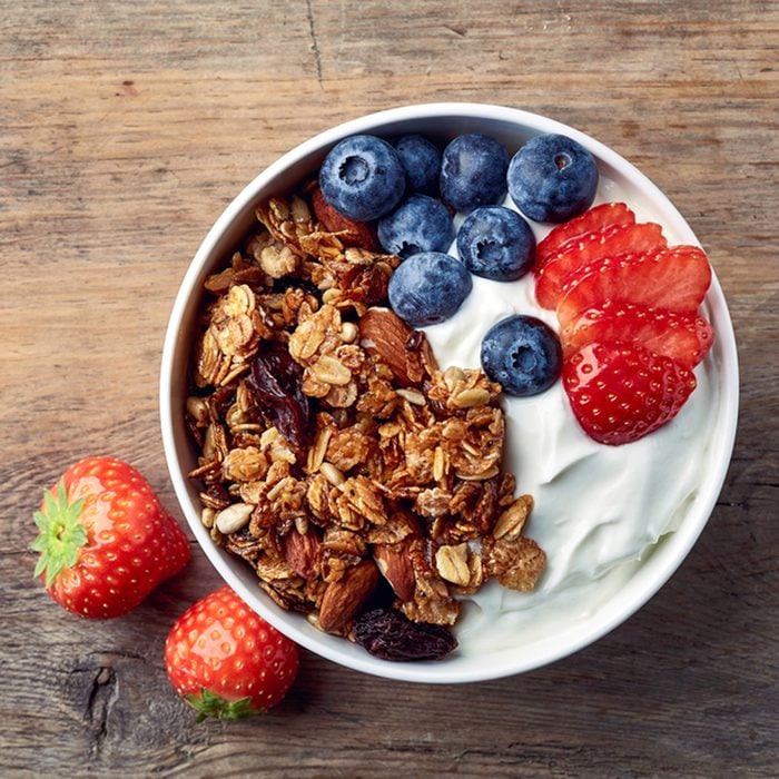 Bowl of homemade granola with yogurt and fresh berries on wooden background from top view