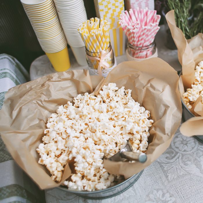 Details of a tasty candy bar with buckets of popcorn and pasteboard pink and yellow glasses