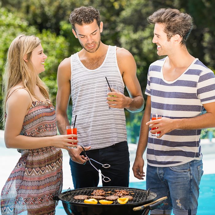 Happy friends talking to each other while preparing barbecue near pool;
