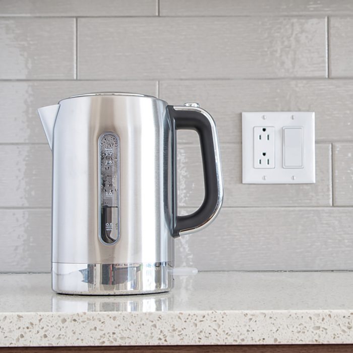 Modern electric stainless steel kettle on a granite counter top against a ceramic background