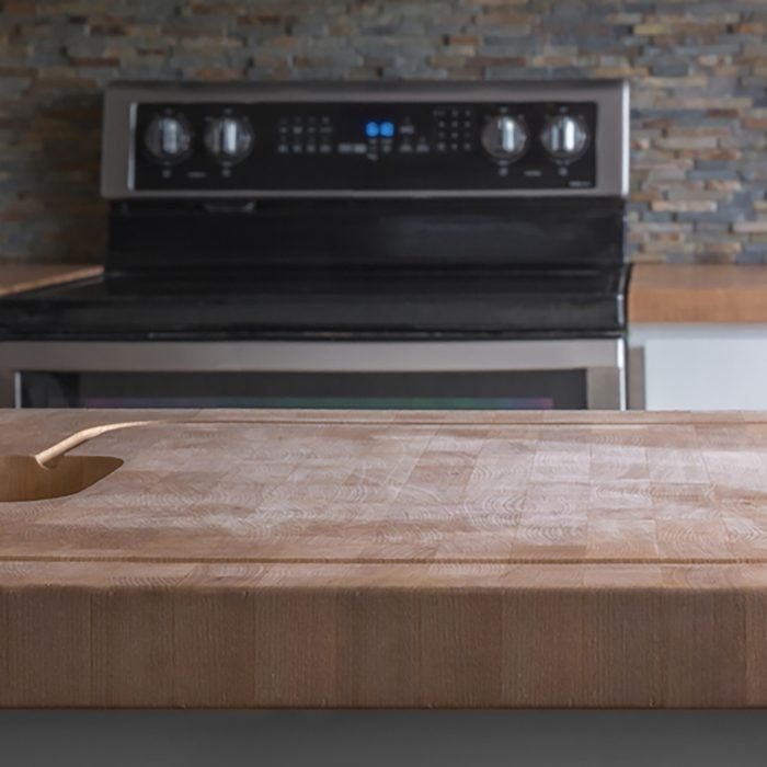 Kitchen Island wood butcher block top with stove, sink and counter in background