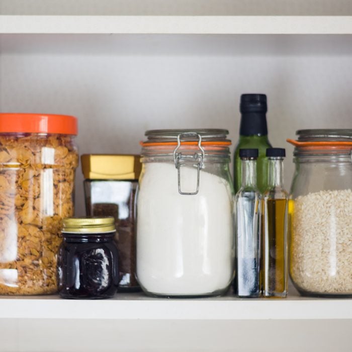 stocked kitchen pantry with food - jars and containers of cereals, jam, coffee, sugar, flour, oil, vinegar, rice