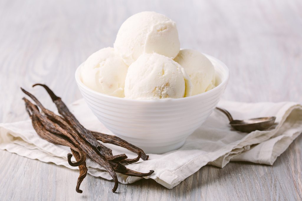 Balls of vanilla ice cream in a white bowl on a wooden background.