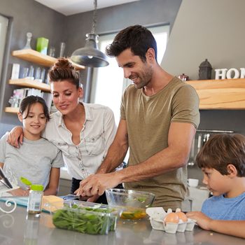 Family In Kitchen Following Recipe On Digital Tablet