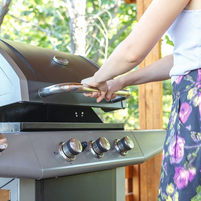 Young woman opens gas grill, prepares grill for BBQ, steak, sausages for happy family holiday.