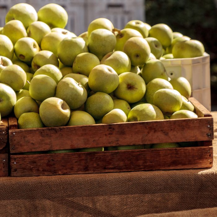 Bushel of green apples in a crate at a farmers market with other fruits and vegetables.