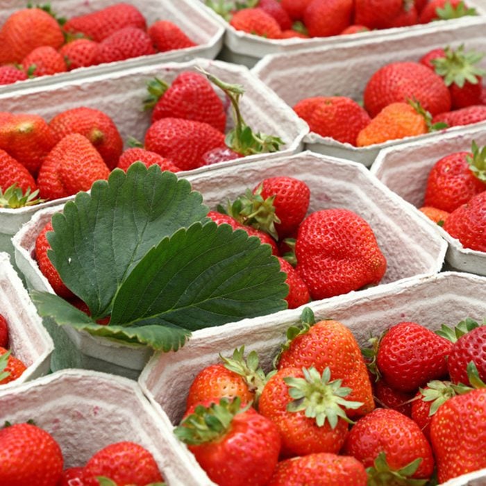Close up red ripe fresh strawberry with green leaves in white cardboard paper crates on retail display of farmers market stall