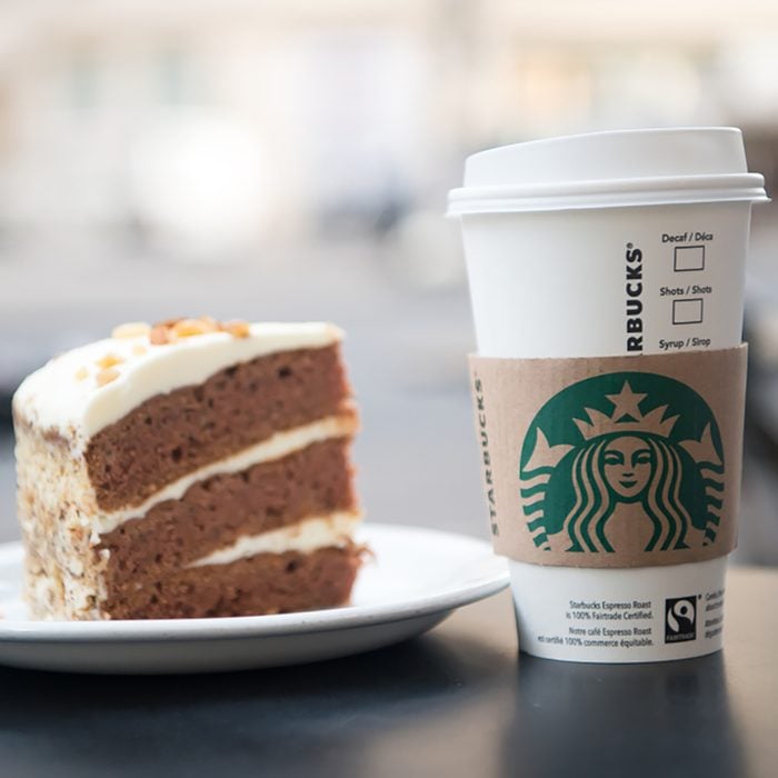 A tall Starbucks coffee in starbucks coffee shop with cake.